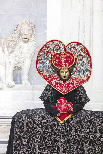 Heart-shaped costume stands in front of a sculpture of a lion at the Venice Carnival