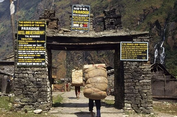 Heavily laden porters enter village gateway