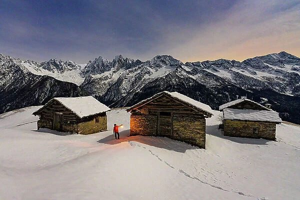 Hiker with lamp admiring the stars over snowy mountains, Tombal, Soglio, Val Bregaglia, Graubunden, Switzerland (MR)