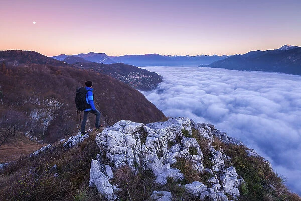 Hiker over the top looks lake Como (ramo di Lecco) covered by the fog at sunrise, Como and Lecco province, Lombardy, Italy (MR)
