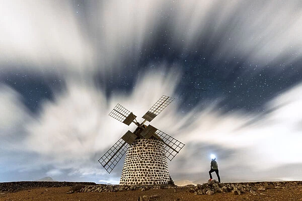 Hiker man with head torch admiring clouds in the starry sky over the windmill, La Oliva