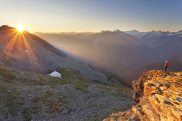Hiker observes the sunrise from the summit of Peterskaopfl, Zillertal Alps, Tyrol