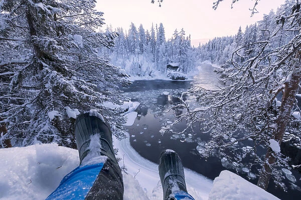 Hiker rests on the snow above Myllykoski rapids, Juuma, Oulanka National Park, Kuusamo