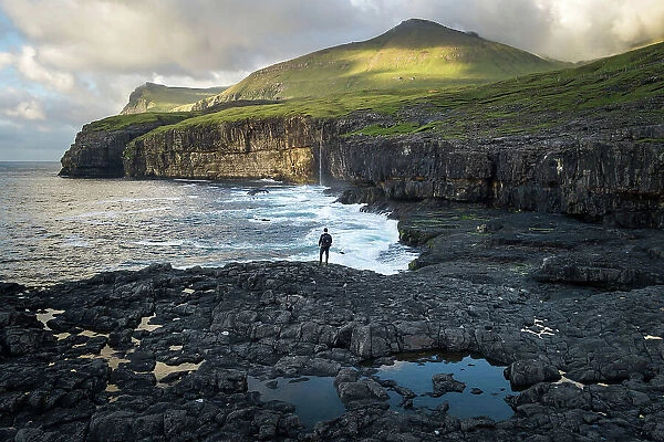 A hiker standing along the coast of the village of Eiði at sunset. Island of Eysturoy. Faroe Islands