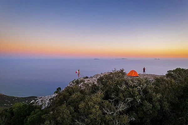 Hiker stands on top of Circeo peak near his tent enjoying the view of Pontine islands, Circeo National Park, Tyrrhenian sea, Mediterranean sea, Latina province, Latium, Italy (MR)