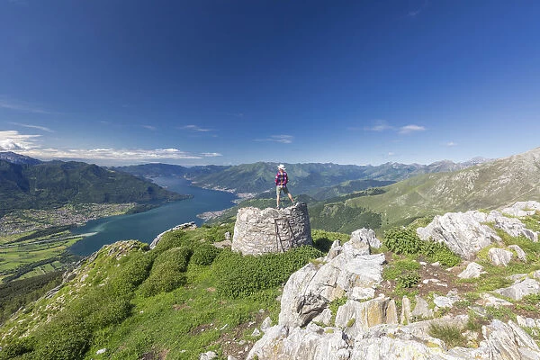 Hiker on summit of Monte Berlinghera looks towards Lake Como, Sondrio province, Lombardy