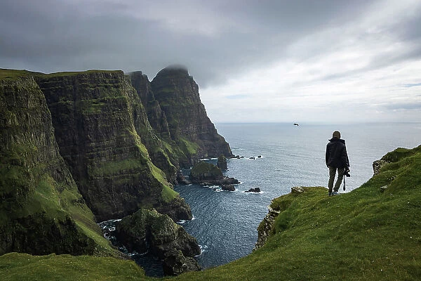 A hiker walking along the huge cliffs on the west coast of the islands of Suðuroy. In the backgound the cliff of Beinisvorð. Faroe Islands