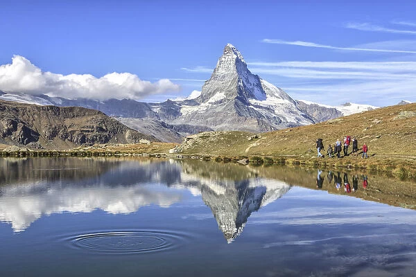 Hikers walking on the path beside the Stellisee with the Matterhorn reflected