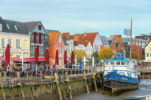 Houses with colorful facades on Hafenstrasse and boat at low tide, Husum, Nordfriesland, Schleswig-Holstein, Germany