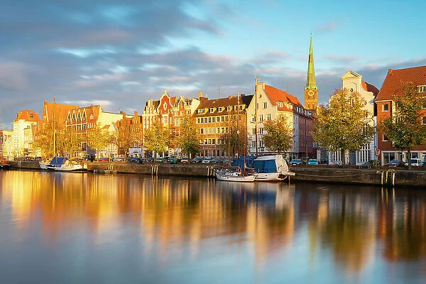 Houses on riverfront of Trave river with tower of St. Jakobi Kirche church in background at sunset, Lubeck, UNESCO, Schleswig-Holstein, Germany