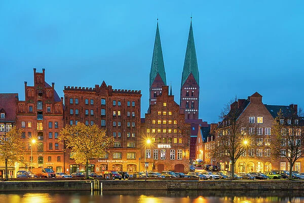 Houses on riverfront of Trave river with towers of St. Marienkirche church in background at twilight, Lubeck, UNESCO, Schleswig-Holstein, Germany