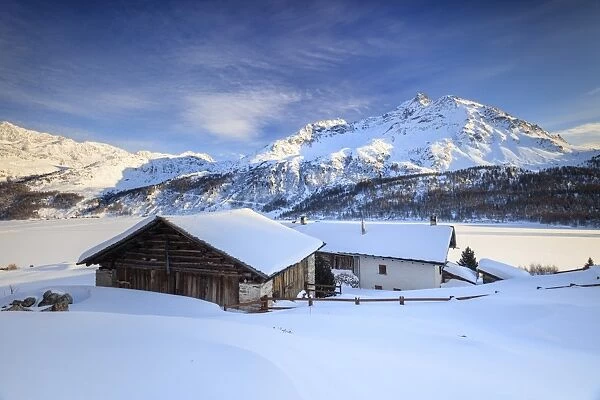 Huts and mountains covered in snow at sunset Spluga Maloja Canton of Graubunden Engadin