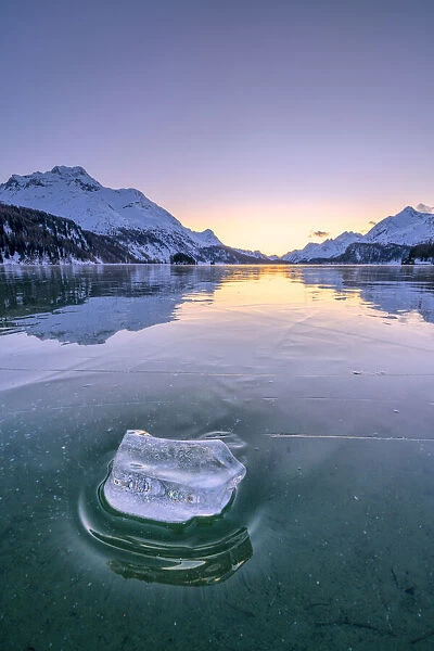 Ice block on frozen water of Lake Sils lit by a cold winter sunset, Graubunden, Engadine