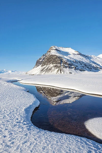 Iceland, Europe. Mountains mirroring in a crystal clear water surrounded by snow
