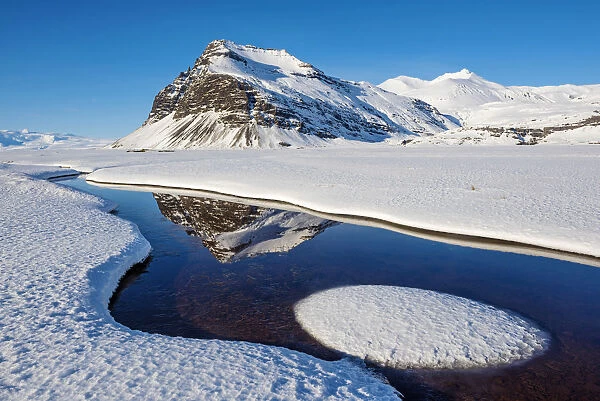 Iceland, Europe. Mountains mirroring in a crystal clear water surrounded by snow