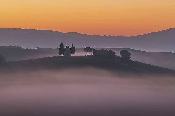 The iconic Chapel of Madonna di Vitaleta appearing through the thick layer of fog. Val d'Orcia, Tuscany, Italy