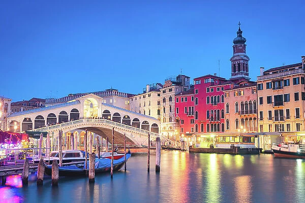 Illuminated buildings and Rialto Bridge reflected in the Grand Canal with moored gondolas at blue hour, Venice, Veneto, Italy
