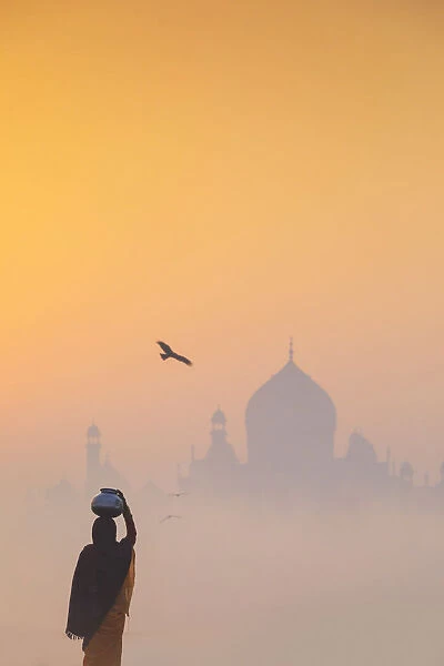 India, water carrying a water pot on a foggy morning with the sun rising on the Taj Mahal
