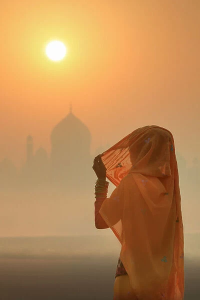India, woman wearing a traditional sari on a foggy morning with the Taj Mahal in