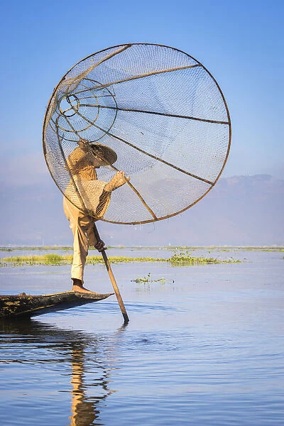 Intha fisherman with a traditional conical fishing net against clear sky, Lake Inle