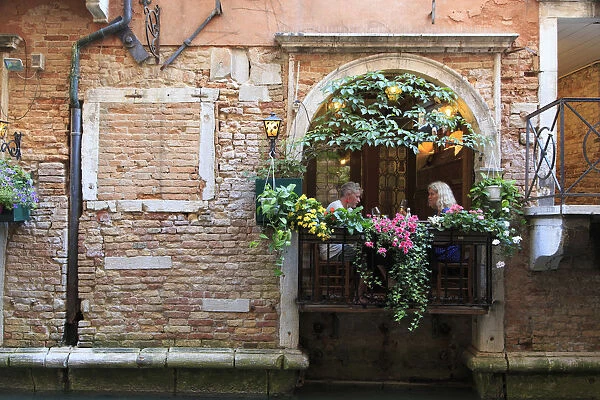 Italy, Veneto, Venice, Sestiere of Rialto, couple eating outdoor by small canal