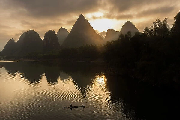 Karst mountains and bamboo fishing raft on Li River at sunrise, Yangshuo, China