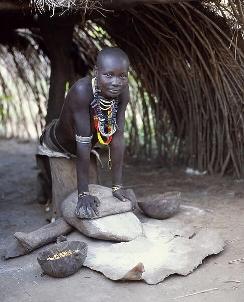 A Kwego woman grinds sorghum flour at the entrance to her hut