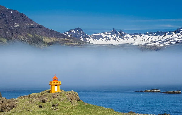 Lighthouse on cliff at Djupivogur against mountain range, East Iceland, Iceland