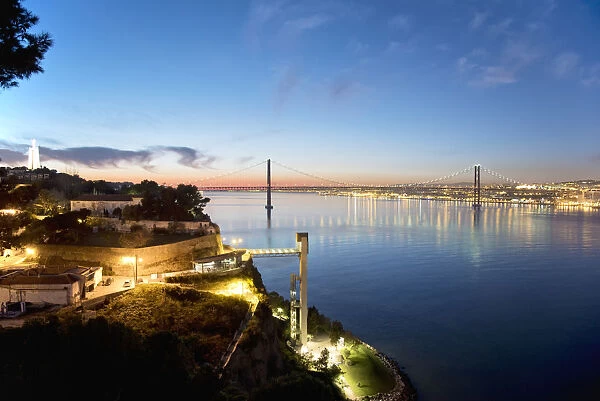 Lisbon and 25 de Abril bridge over the Tagus river, at dusk, seen from Almada. Portugal
