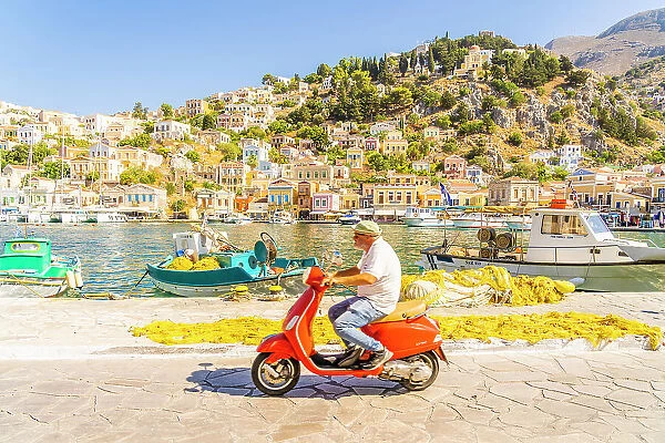 A local man riding a red Vespa in the colourful harbour in Symi, Dodecanese Islands, Greece