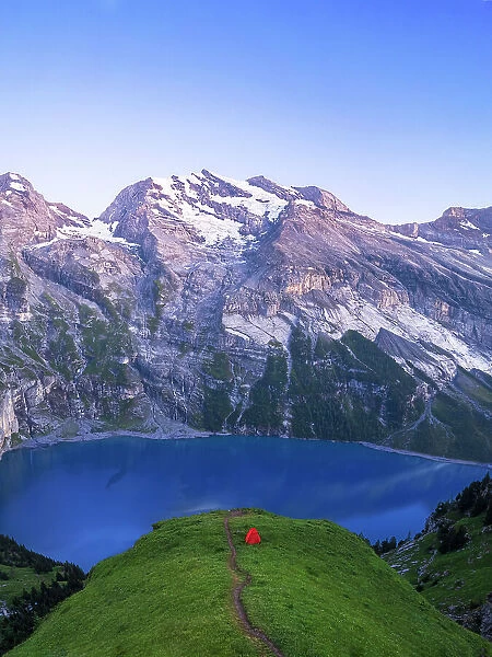 A lone tent on top of a hill surrounding the lake of Oeschinensee at dusk, Bernese Oberland, Kandersteg, Switzerland