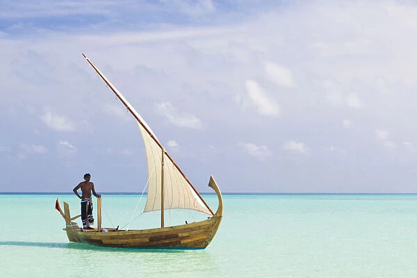 Maldives, Rasdhoo Atoll, Kuramathi Island. A Maldivian man sails a traditional Dhoni. MR