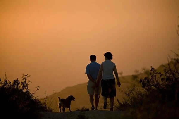 Malta, Dingli, Europe; A couple walking their dog on Dingli Cliffs during sunset