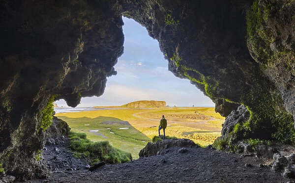 A man observes Dyrholaey cliff from a cave during summer, Vik I Myrdal, southern Iceland