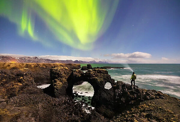 A man observes Gatklettur arch and northern lights, Arnarstapi, Snaefellsnes peninsula, Vesturland region, Iceland
