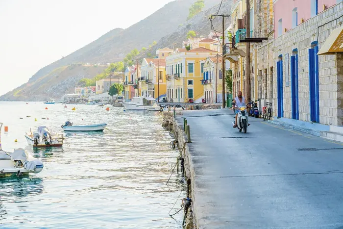 Framed Print : A man riding a motor cycle by the colourful harbour in Symi, Dodecanese Islands, Greece Framed Print : A man riding a motor cycle by the colourful harbour in Symi, Dodecanese Islands, Greece