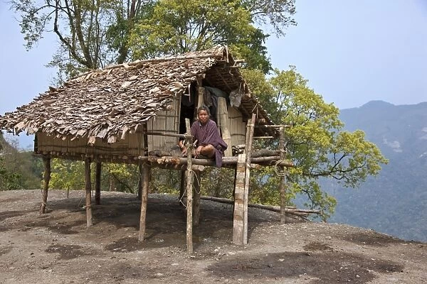 A man sits on the veranda of his small house, raised on stilts, situated precariously on the edge of a