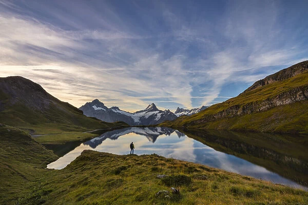A man stands in front of Bachalpsee and mountains during sunrise, Jungfrau region