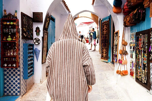 Man with traditional Djellaba looking at the gift shops in the street markets of Chefchaouen, Morocco