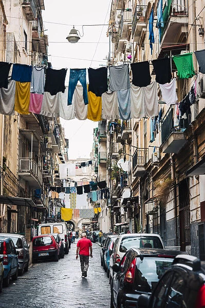 Man walks in an alley in Naples, with clothes hanging between the buildings