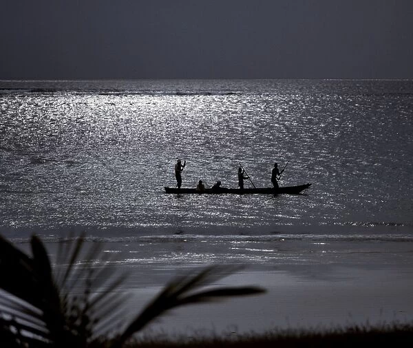 Three men pole a dugout canoe by moonlight in shallow water along Diani Beach