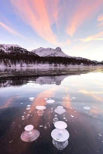 Methane bubbles in the icy surface of Silsersee with snowy peak illuminated by sunset