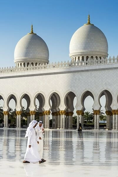 Two Middle Eastern men traditionally dressed walking in the courtyard of the Sheikh Zayed Mosque