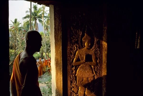 Monk standing by the door of Wat Mai Suwannaphumaham