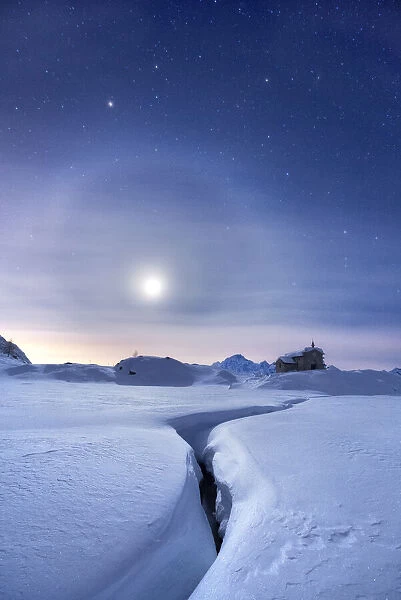 Moon halo in the night sky above a traditional mountain church during a winter full moon