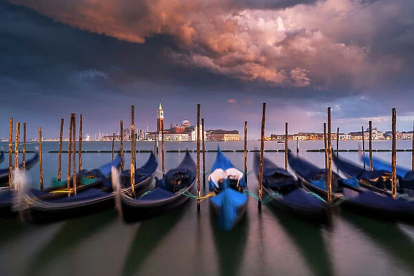 Moored gondolas under a stormy sky at sunset with San Giorgio Maggiore island in the background, Venice, Veneto, Italy