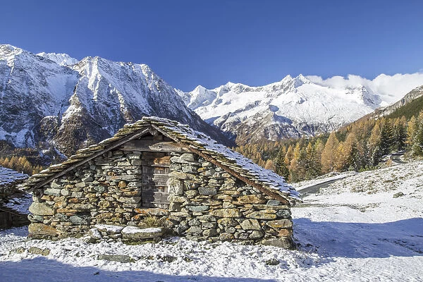 A mountain hut surrounded by snow capped peaks and colorful woods in autumn at Alp Entova