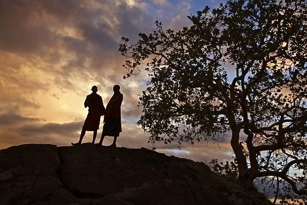 Two Msai men silhouetted on a hill at sunset