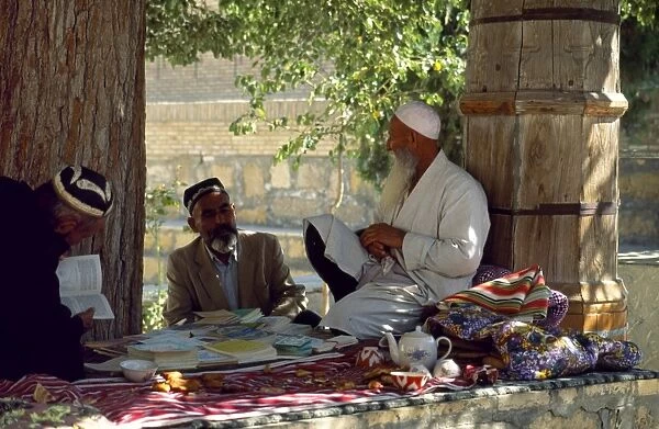 A mullah sits benath a tree outside the Mausoleum of