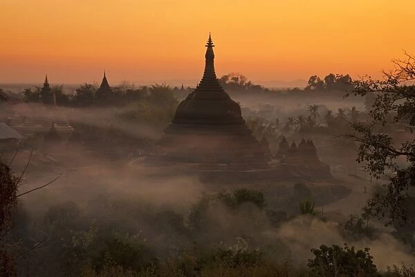 Myanmar, Burma, Mrauk U. Evening mist and smoke from village cooking fires swirl around Ratanabon Paya, Mrauk U
